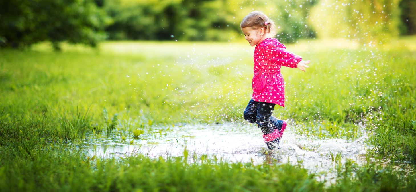 Little girl jumping in the mud puddle laughing