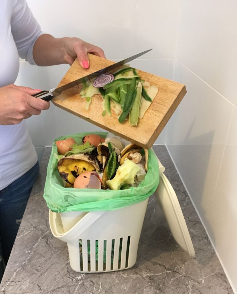 Person putting food scraps into a small, in-house compost bucket.